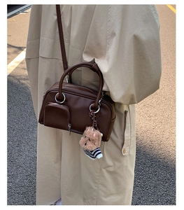 Detail of dark brown leather Boston bag with dog charm and embossed logo on front pocket