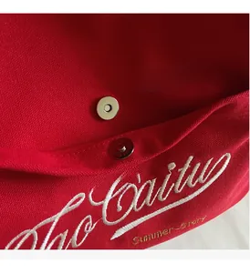 Detail of red canvas bag featuring white letter embroidery and silver magnetic closure