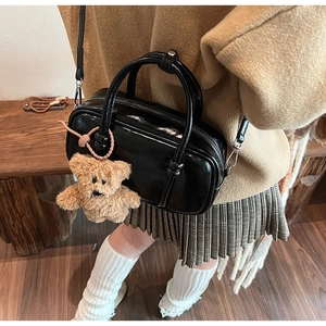 Detail of black patent leather bowling bag with brown plush bear charm and silver hardware