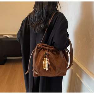 Detail view of large dark brown suede bucket bag with wooden bead fringe on shoulder