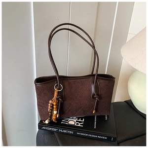 Detail of dark brown quilted suede tote bag featuring wooden bead tassel and leather handles