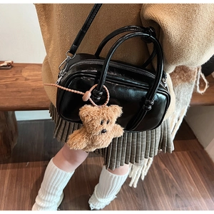 Close-up of a shiny black bowling handbag with a cute plush bear charm decoration