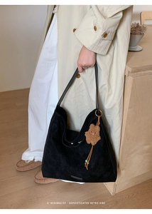 Close-up of black suede tote bag with metal nameplate and cute brown plush bear charm