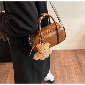 Detail of a brown leather bowling bag with cute plush bear charm and crossbody strap