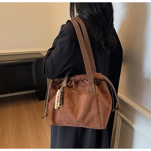 Detail of a brown suede bucket bag with colorful beaded tassels and drawstring closure