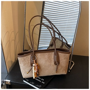 Close-up of brown quilted tote bag with wooden bead charm and suede texture