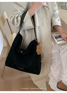Detail of minimalist black oversized tote bag featuring a plush brown pompom charm and gold hardware