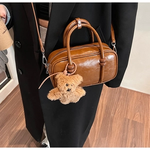 Detail of vintage brown leather bowling bag with plush bear charm and brand logo