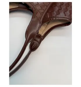 Close-up of woven dark brown leather tote bag showing reinforced handle stitching and lining