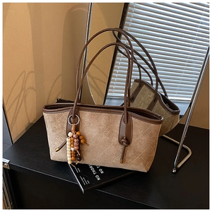 Close-up of khaki quilted tote bag featuring a wooden bead tassel and sleek brown handle