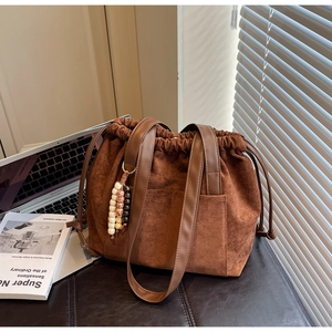 Detail of brown faux suede bucket bag featuring drawstring closure and wooden bead charm