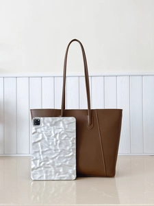 Detail of dark brown pebble leather tote bag featuring fine stitching and slim shoulder straps