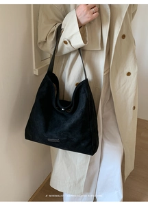 Close-up of minimalist black suede tote bag with metal logo on beige trench coat