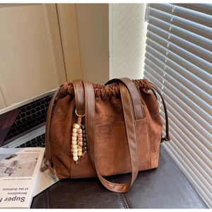 Detail of brown suede bucket bag with wooden bead charm and leather shoulder straps