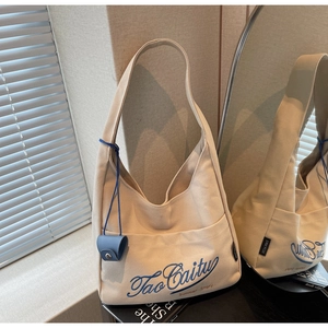 Detail of beige canvas tote bag with blue embroidery and matching mini pouch accessory