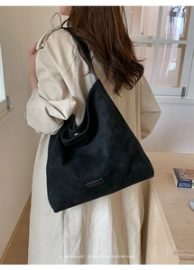 Close-up of minimalist black suede tote bag with metal logo on a beige trench coat