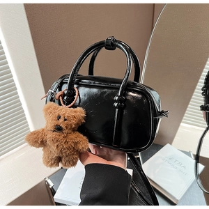 Detail showing glossy black PU leather bowling bag with brown plush bear charm and handles