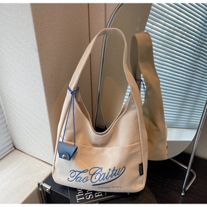 Detailed close-up of beige canvas tote bag with blue embroidery and side leather charm
