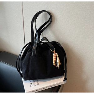 Detail of black suede drawstring tote featuring a vintage beaded tassel and leather handle