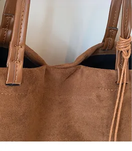 Detail of suede tote bag showing brown stitching and smooth leather handle joints