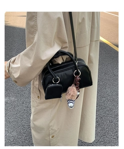 Outdoor street shot of a vintage black leather crossbody bag with a plush doll charm