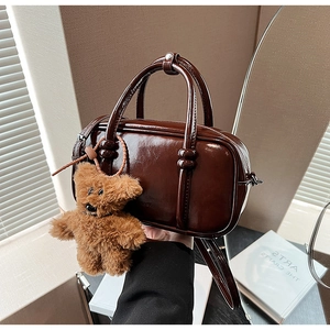 Close-up of glossy brown leather bowling bag with cute teddy bear charm and knotted handles
