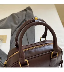 Macro view of a dark brown leather Boston bag featuring rounded handles and gold hardware
