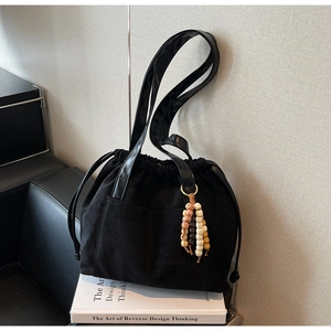 Detail of black drawstring bucket bag with decorative ceramic bead tassel on shoulder strap