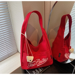 Close-up of red canvas tote bag with TaoCaitu embroidery and small cream pouch charm