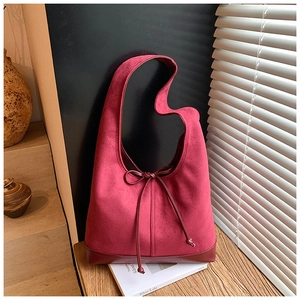 Gros plan du sac porté épaule en daim rouge foncé avec finitions cuir sur table en bois