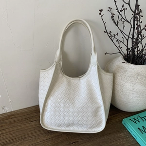 Detailed view of cream woven leather tote bag texture on a minimalist wooden surface