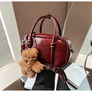 Detail of burgundy glossy PU leather bowling bag with cute plush bear charm decoration