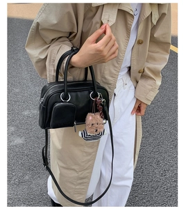 Detail of a black leather Boston bag featuring a front pocket and cute bear charm accent