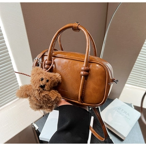 Detail of a brown leather Boston bag with sphere knots and plush bear charm