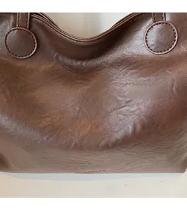 Detailed macro view of chocolate brown oil-wax leather tote with golden brand logo