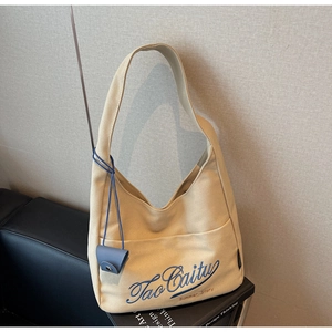 Close-up of beige canvas bucket bag with blue embroidery and leather pendant detail