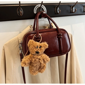 Close-up of a burgundy vintage bowling bag with a plush bear charm on a trench coat