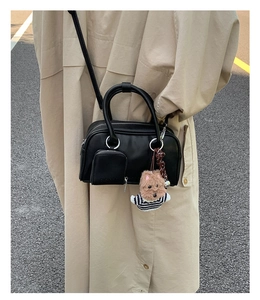 Detail of a black leather mini boston bag with metal handle and cute teddy bear charm