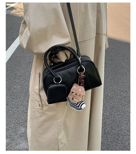 Detail of black leather crossbody bag with a cute plush dog charm and mini pouch