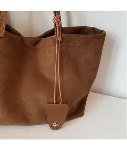 Detail view of a large brown suede tote bag featuring unique creative leather pendants
