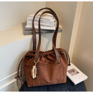 Detail of suede drawstring bucket bag with decorative beaded tassel and front pocket