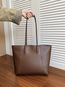 Detail of a large brown faux leather tote bag with V-shaped stitching held by a person