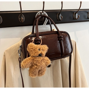 Detail of dark brown glossy purse with CUEARCK branding and teddy bear pendant
