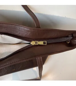 Detail of dark brown leather tote featuring golden zipper and brand logo engraving