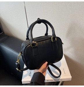 Detail of minimalist black handbag showing smooth matte leather and gold-toned hardware