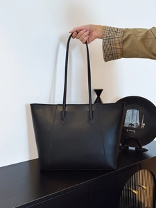Detail of a minimalist black leather tote bag with long shoulder straps for office wear