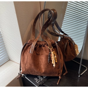 Detail of brown suede bucket bag featuring beaded tassel and smooth leather handle