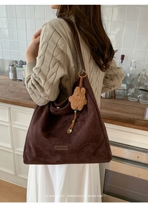 Detail of suede tote bag with leather logo tag and cute plush bear charm on side