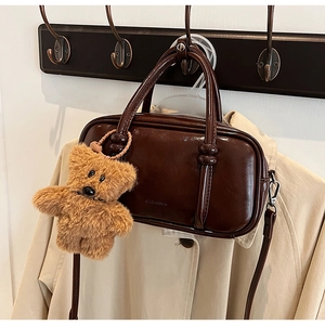 Detail of dark chocolate patent leather handbag with a plush bear charm on a coat rack