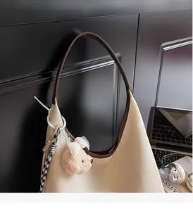 Détail du sac bandoulière en toile beige avec bordure en cuir et porte-clés ours